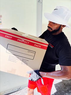 Worker in white hard hat and black shirt holding red fragile package box