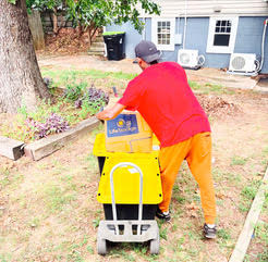Person in red shirt and yellow pants operating yellow and black lawn equipment in residential yard
