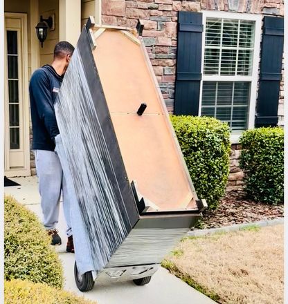 Man carrying large wooden door panel toward brick house entrance