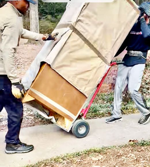 Two workers carefully tilting a wrapped refrigerator on a dolly during delivery