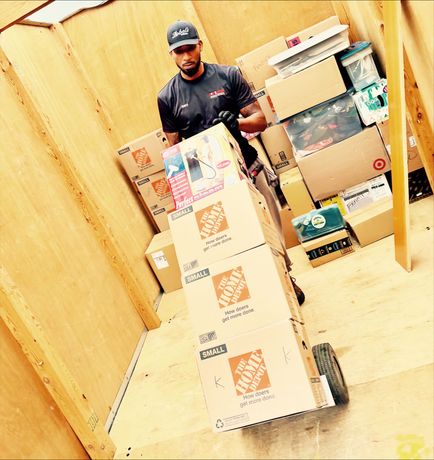 Worker in hard hat organizing cardboard boxes on wooden floor inside construction space