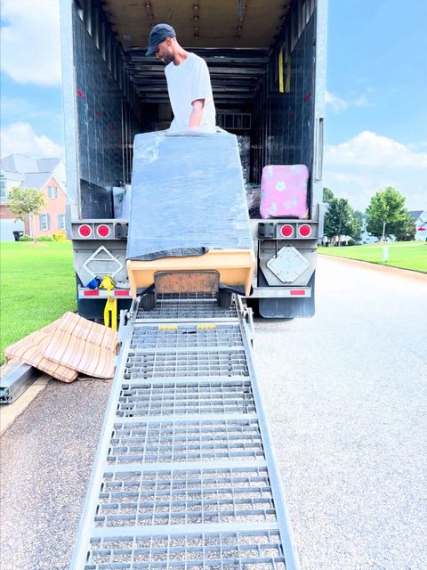 Moving truck with ramp extended, worker loading wrapped furniture and boxes